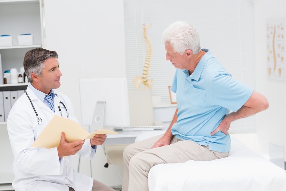 Male doctor discussing reports with senior patient suffering from back pain in clinic