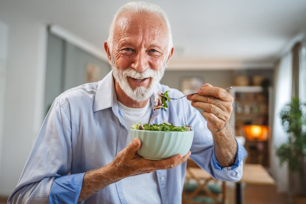 Älterer Mann isst einen frischen Salat als Teil einer bewussten Ernährung bei Gicht.